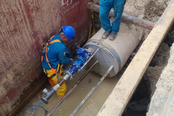Trabajadores realizando mantenimiento e instalación de válvula en tubería subterránea de gran diámetro en obra de infraestructura hidráulica y redes de acueducto.